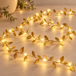 Può includere: Una ghirlanda flessibile di foglie metalliche dorate intrecciate con piccole luci LED bianco caldo. Il filo a forma di vite presenta foglie testurizzate e appuntite distanziate uniformemente lungo il cavo, creando un effetto luminoso.