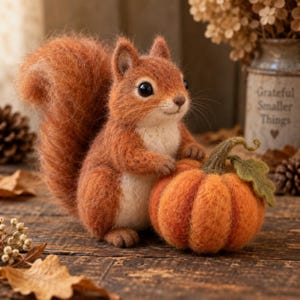 May include: A needle-felted squirrel figurine with reddish-brown fur and a cream-colored chest, holding a small orange felted pumpkin with a green stem and leaf. The squirrel has dark eyes, a small nose, and a large, fluffy, textured tail.