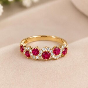 May include: A gold band ring featuring a wavy design set with five round-cut vibrant red stones and small clear white stones arranged in a delicate pattern along the top half of the band, creating a continuous sparkling effect across the metal surface.