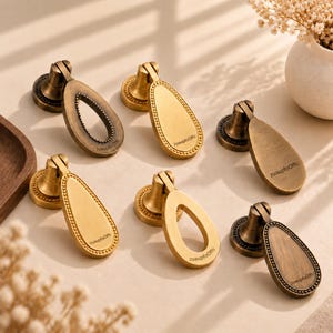 May include: Six brass-toned metal furniture pulls with a teardrop shape and beaded edges. Each pull features a circular mounting base and a hinged drop handle. The text "zuaupfoOffc" is engraved on the surface of each piece in a small font.