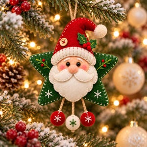 Könnte beinhalten: Ein sternförmiger Weihnachtsanhänger aus Filz mit einem Weihnachtsmann-Gesicht, weißem Bart, roter Mütze mit Holzknopf und grünen Stechpalmenblättern. Drei hängende Filzkugeln in Rot und Weiß sind mit Stickereien an der Unterseite befestigt.