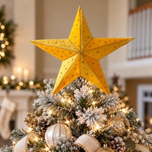 May include: A five-pointed star tree topper in a vibrant golden yellow hue, featuring a subtle textured surface with small, delicate star-shaped cutouts that allow light to pass through, positioned atop a flocked green Christmas tree.
