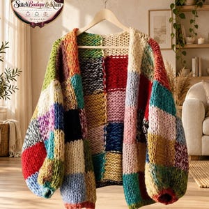 May include: A chunky knit cardigan featuring a patchwork design with large squares in various colours including red, blue, yellow, green, pink, and cream. The garment has long sleeves, a relaxed fit, and is displayed on a wooden hanger.