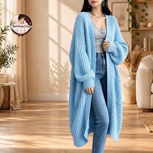 May include: A long, light blue open-front cardigan made of a thick, ribbed knit fabric. The garment features long, loose sleeves and two front pockets. It is worn over a grey tank top and blue denim jeans, creating a casual, layered appearance.