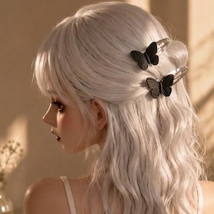 May include: A person with wavy platinum blonde hair styled with two black butterfly hair clips. The person wears a cream-colored ribbed camisole top and a matching knitted cardigan draped over the shoulders. The text PeachybyRyn is visible.