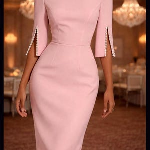 May include: A light pink knee-length dress featuring a boat neckline, fitted bodice, and three-quarter length sleeves. The sleeves have a vertical slit detail along the outer edge, which is lined with small white pearls along both sides of the opening.