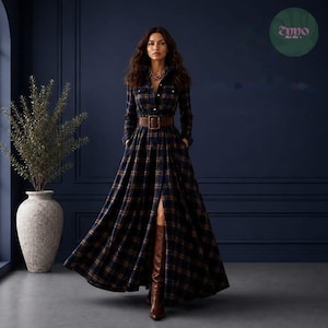 May include: A long-sleeved, floor-length plaid dress in navy blue, brown, and orange tones. The dress features a collared neckline, a button-down front, and a brown leather belt with a rectangular buckle at the waist. Brown leather boots are visible.