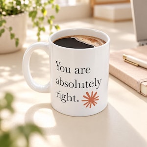 May include: A white ceramic mug filled with black coffee, featuring the black printed text "You are absolutely right." and a small, rust-colored starburst graphic on the side. The mug has a curved handle and a smooth, glossy finish.
