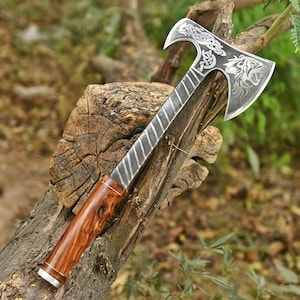 May include: A double-bit axe featuring a polished metal head with intricate Celtic knotwork and a roaring tiger engraving. The handle is crafted from polished brown wood with a diagonal striped pattern near the head and a silver-toned base.