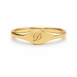 Pode incluir: Um anel de sinete em ouro polido com uma face oval lisa e plana. O centro da face do anel está gravado com uma letra D maiúscula elegante em cursivo. A banda é de ouro maciço com um perfil arredondado e um acabamento de alto brilho.