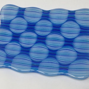 May include: A blue and white glass soap dish with a wavy edge and a pattern of horizontal stripes.
