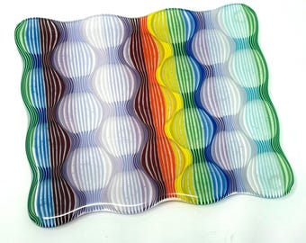 May include: A colorful, wavy glass dish with a striped pattern. The dish features vertical stripes in shades of blue, green, yellow, orange, and purple. The design creates a textured, bubble-like effect. The edges are smooth and the overall shape is rectangular.