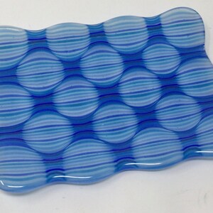 May include: A blue and white glass dish with a wavy edge and a pattern of horizontal stripes. The dish is made of clear glass with a blue and white striped pattern.