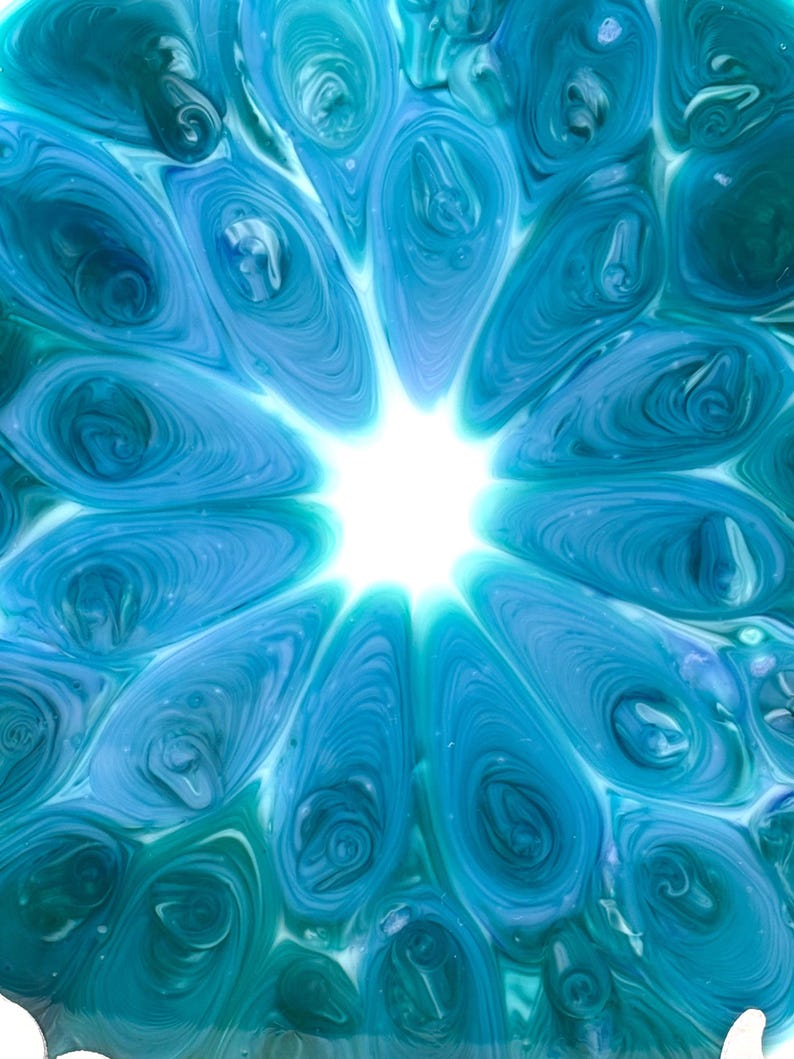 May include: Abstract artwork featuring a central bright white light surrounded by swirling patterns of blue and teal. The design resembles a stylized flower or starburst, with a fluid, organic feel.
