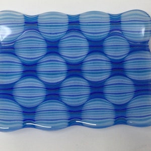 May include: A blue and white glass dish with a wavy edge and a pattern of horizontal stripes. The dish is made of clear glass with a blue and white striped pattern.