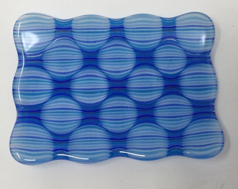 May include: A blue and white glass dish with a wavy edge and a pattern of horizontal stripes. The dish is made of clear glass with a blue and white striped pattern.