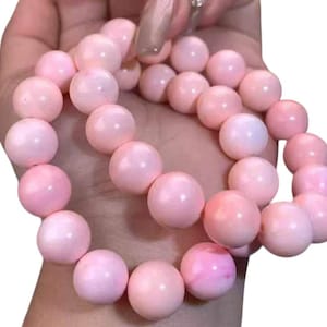 May include: A bracelet composed of smooth, round, light pink beads with a subtle pearlescent sheen. The beads are uniform in size and strung together in a circular shape, creating a continuous loop of soft, pastel-colored spherical elements.
