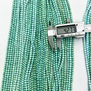 May include: Multiple strands of small, round, turquoise-colored beads with natural veining. A digital caliper is positioned over one bead, displaying a measurement of 4.27 mm, confirming the diameter of the individual beads in this collection.
