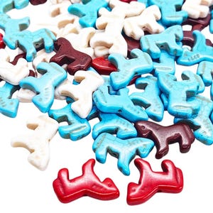 May include: A collection of small, horse-shaped beads in various colors including turquoise, white, red, and dark brown. The beads are scattered across the frame, with some arranged in a vertical line on a thin metal wire, showing a uniform shape.