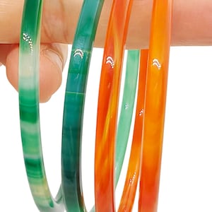 May include: Four thin, smooth bangles in shades of green and orange. Two bangles are green with translucent bands, and two are orange with marbled patterns. Each bangle features small, silver-colored crescent moon accents. Text reads GREEN and KEI.