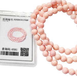 May include: A light pink beaded necklace consisting of smooth, spherical beads. Beside the necklace is a white rectangular jewellery identification certificate with black text, a QR code, and a red circular stamp, stating a total weight of 36.37g.