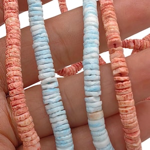 Può includere: Due fili di perline a forma di disco, un filo caratterizzato da un colore arancione corallo testurizzato e l'altro filo con un motivo marmorizzato azzurro cielo e bianco. Le perline sono infilate su un sottile cordino rosso.