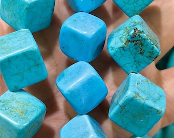 May include: A collection of bright turquoise blue beads shaped like cubes. The beads feature a smooth, polished finish with some displaying natural dark brown veining patterns across their surfaces, arranged in multiple vertical strands.