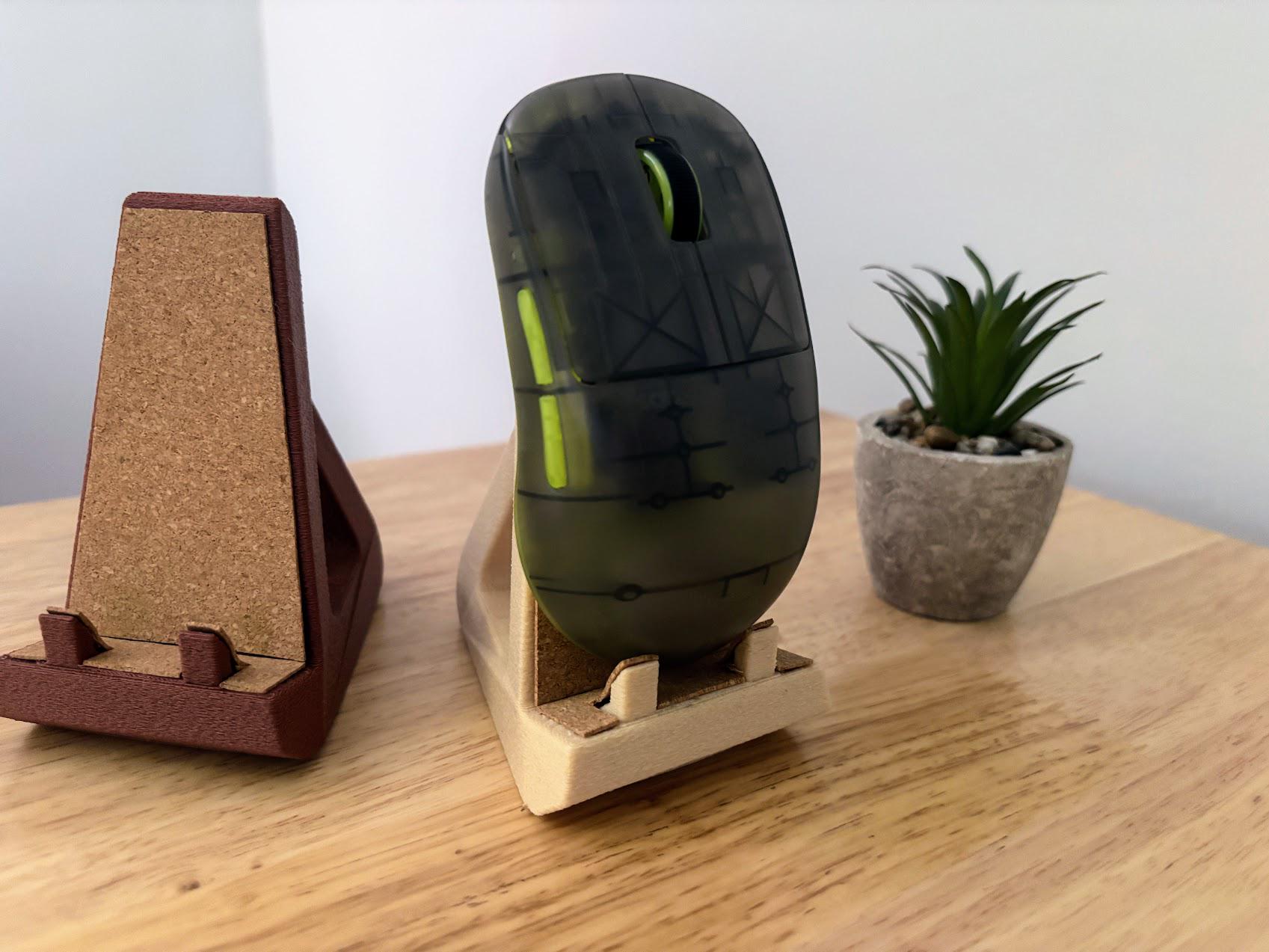 May include: A translucent dark olive computer mouse with a bright lime green scroll wheel, resting on a beige stand with a cork insert. Beside it sits an empty dark brown stand with a cork insert, featuring a triangular frame design.