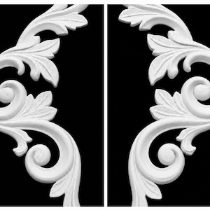 May include: Two white decorative architectural ornaments featuring symmetrical acanthus leaf carvings and scrollwork patterns. These molded pieces display intricate botanical details with curved lines and raised textures against a black background.