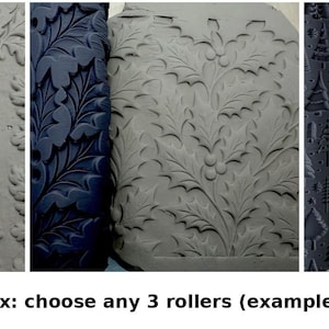 May include: Three cylindrical clay texture rollers with dark blue surfaces, each featuring a distinct embossed pattern: one with oak leaves and acorns, one with holly leaves and berries, and one with a variety of stylised pine trees.