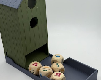 May include: A green and gray plastic dice tower shaped like a small house with a rectangular tray base. Five light-colored wooden dice are resting in the tray, each featuring colorful printed icons of fish, berries, and wheat stalks on their sides.