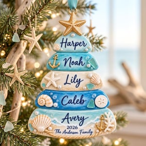 May include: A coastal-themed Christmas tree ornament shaped like a stacked pyramid, featuring five blue and white tiers decorated with seashells, starfish, and gold anchors. The names Harper, Noah, Lily, Caleb, and Avery are printed in dark blue script.