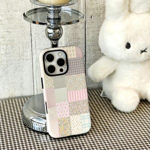 May include: A smartphone case featuring a patchwork design of various pastel-coloured patterns, including floral prints, pink and white stripes, light blue and white checks, and polka dots, with a black camera cutout frame on the upper left side.
