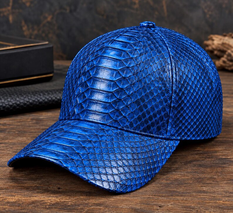 May include: A vibrant blue baseball cap featuring a detailed, raised scale texture across the entire surface. The cap has a structured crown, a curved brim, and a small button at the top centre, showcasing a consistent, glossy finish throughout.