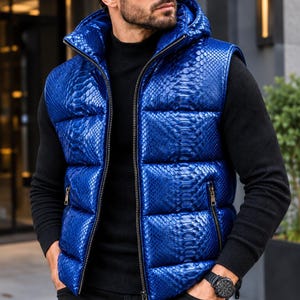 May include: A bright blue puffer vest featuring a textured snakeskin pattern, a hood, and a full-length front zipper. The garment includes two side pockets with metallic zippers, providing a distinct look with its quilted, padded construction.