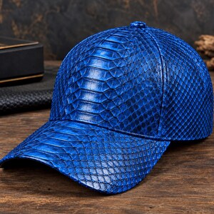 May include: A vibrant blue baseball cap featuring a detailed, raised scale texture across the entire surface. The cap has a structured crown, a curved brim, and a small button at the top centre, showcasing a consistent, glossy finish throughout.