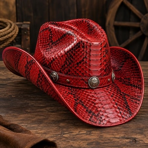 May include: A red cowboy hat featuring a textured snakeskin pattern across the crown and brim. The hat includes a matching red band adorned with three circular silver-toned metal studs, each embossed with a five-pointed star design.