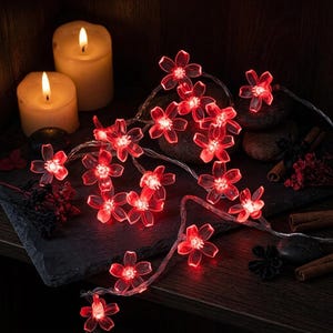Puede incluir: Una cadena de luces LED con cubiertas translúcidas en forma de flor roja. Cada flor tiene cinco pétalos y una fuente de luz central. Las flores están conectadas por un cable fino y flexible, creando un efecto de iluminación.
