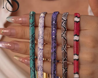 May include: Five flat herringbone chain necklaces featuring various snake skin patterns in teal, light purple, dark purple, brown, and a red, white, and black striped design. Each metal chain has a smooth, reflective finish.