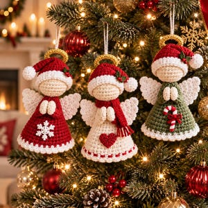 Puede incluir: Tres adornos de ángeles de ganchillo colgados en un árbol de Navidad. Cada ángel lleva un gorro de Papá Noel rojo con halo dorado, alas blancas y un vestido. Un vestido es rojo con un copo de nieve blanco, uno blanco con un corazón rojo y uno verde con un bastón de caramelo.