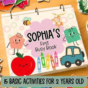 May include: A spiral-bound busy book with a white cover featuring the text Sophia's First Busy Book. The cover displays colorful cartoon illustrations of a bee, a monkey, a red apple, a blue car, and five crayons, all with smiling faces.