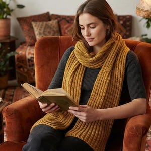 May include: A long, mustard yellow knitted scarf with a vertical ribbed texture, worn draped around the neck over a dark gray short-sleeved ribbed top. The scarf features a thick, chunky yarn construction with visible knit stitches throughout the fabric.