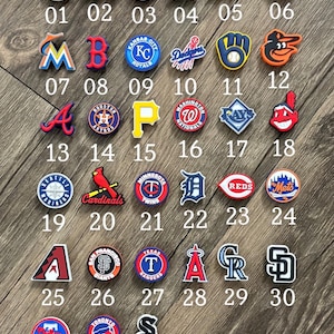 May include: A collection of thirty-three colorful rubber shoe charms featuring various Major League Baseball team logos and baseball-themed icons, each labeled with a corresponding number from 01 to 33, arranged in rows under the title Baseball.