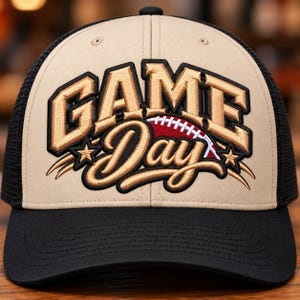 May include: A tan and black trucker hat featuring embroidered text that reads GAME DAY in gold with black outlines. A red football graphic with white laces is positioned between the words, flanked by two gold embroidered stars on each side.