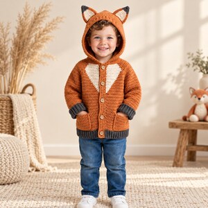 May include: A crochet fox-themed hooded cardigan in burnt orange with a cream-colored chest panel, dark gray sleeve cuffs and hem, and two front pockets. The hood features pointed fox ears with cream accents and five wooden buttons.