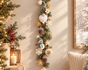 May include: A vertical wall hanging featuring a crocheted gnome and snowman connected by a green garland. The decoration includes crocheted stars, snowflakes, pinecones, and small round ornaments in shades of green, white, and gold, suspended from a wooden rod.
