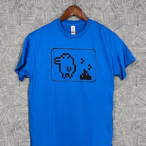 May include: A bright blue t-shirt with a black pixelated image of a bird pooping. The image is inside a black rectangle.