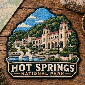 May include: An embroidered patch featuring the Hot Springs National Park bathhouse architecture with cream-colored buildings, red roofs, green trees, and a blue fountain with steam. The text reads HOT SPRINGS NATIONAL PARK in bold letters.