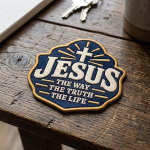 May include: A navy blue embroidered patch with a gold border. The patch features a white cross icon above the word JESUS in large white letters. Below, the text reads THE WAY THE TRUTH THE LIFE in white, all set against a dark blue background.