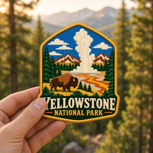 May include: An embroidered patch featuring a brown bison in a landscape with a geyser, mountains, and pine trees. The text YELLOWSTONE NATIONAL PARK is stitched in white and yellow on a dark green background with a gold border.